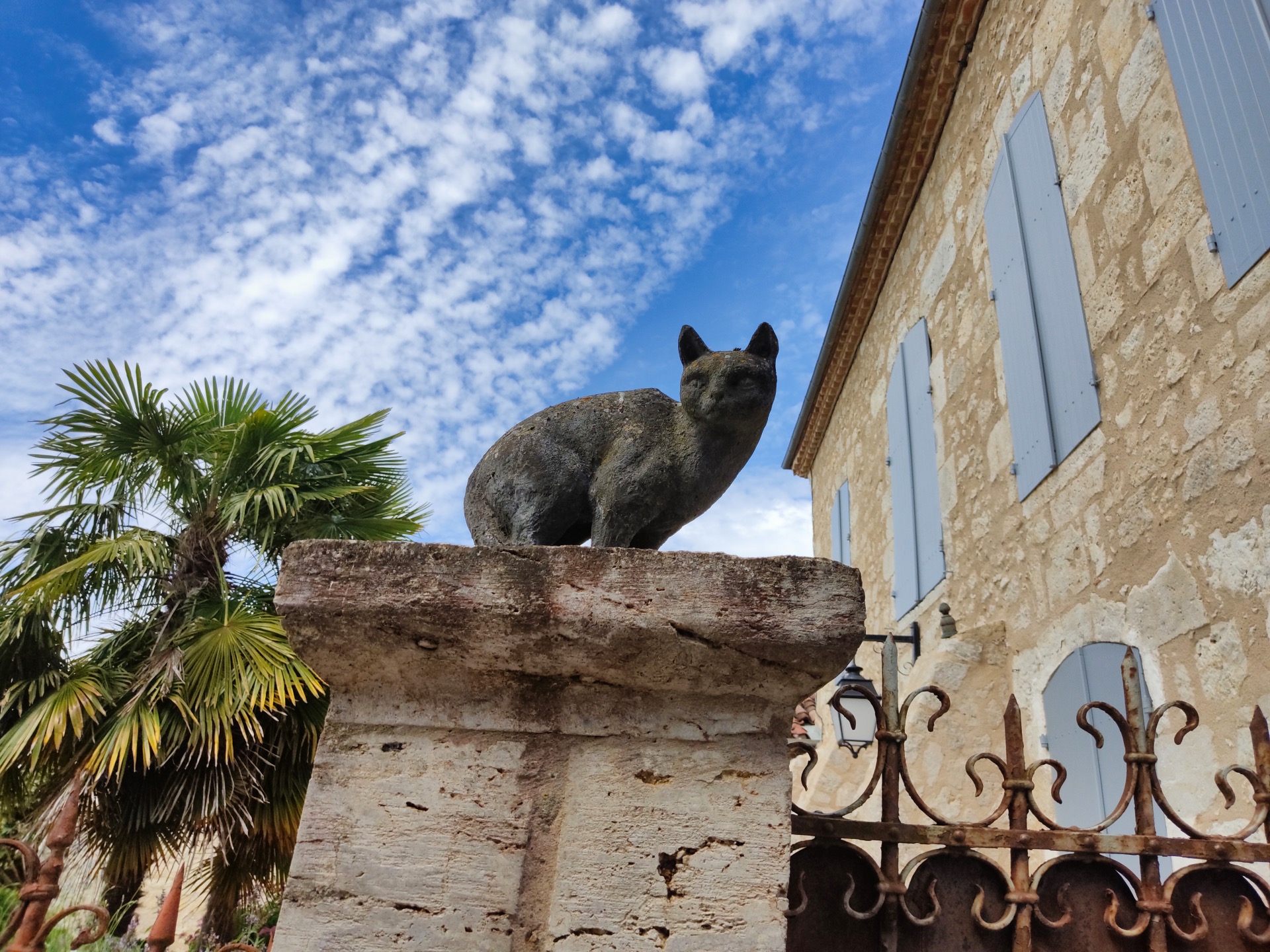 Chat de pierre noirci sur un pilier, à l'entrée d'une propriété à La Romieu