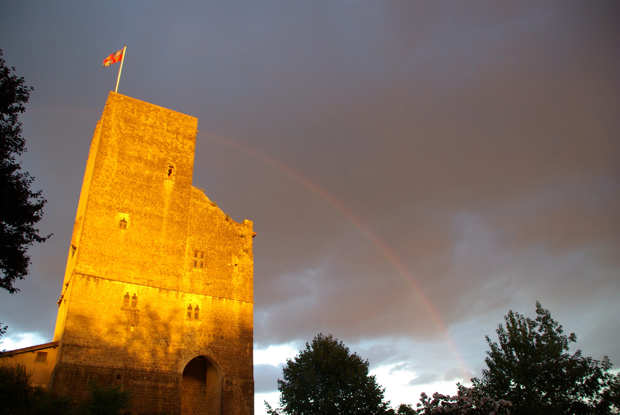Tour de Termes-d’Armagnac dorée sous un arc-en-ciel et un ciel d’orage