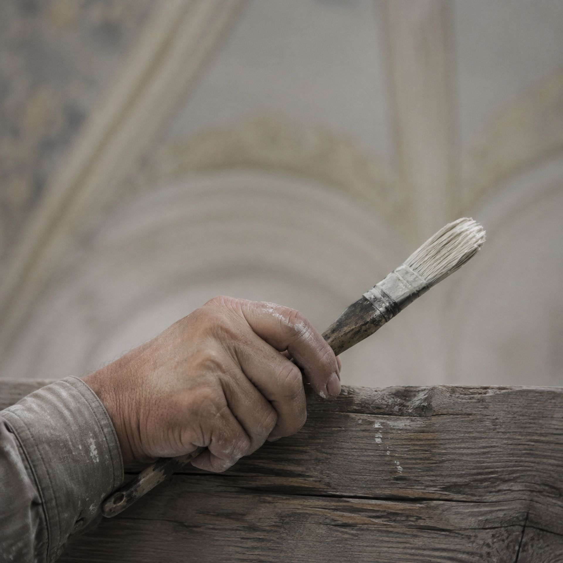 Main d’un peintre tenant un pinceau sur une planche d’échafaudage