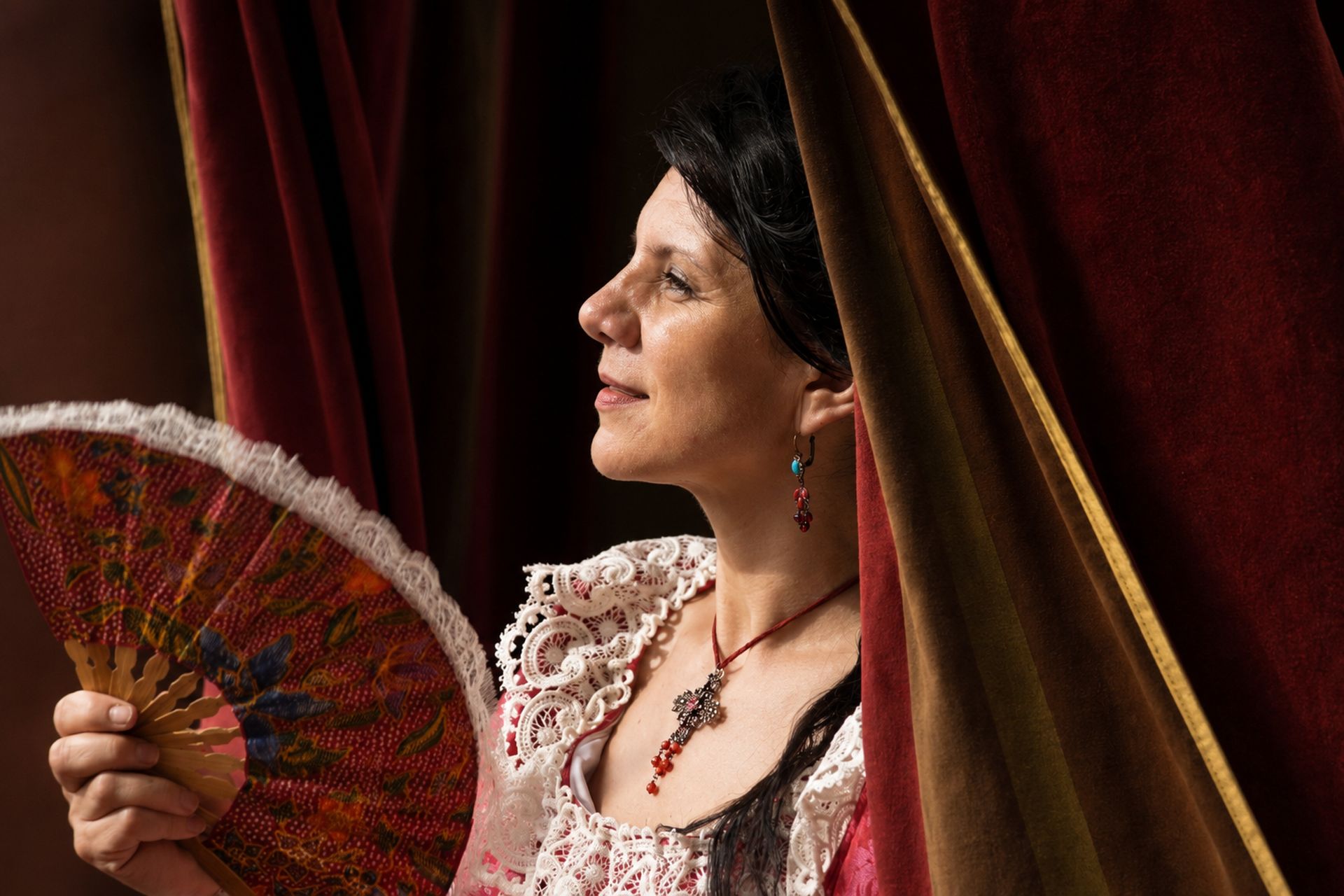 Dame en costume rouge tenant un éventail près d'une tenture