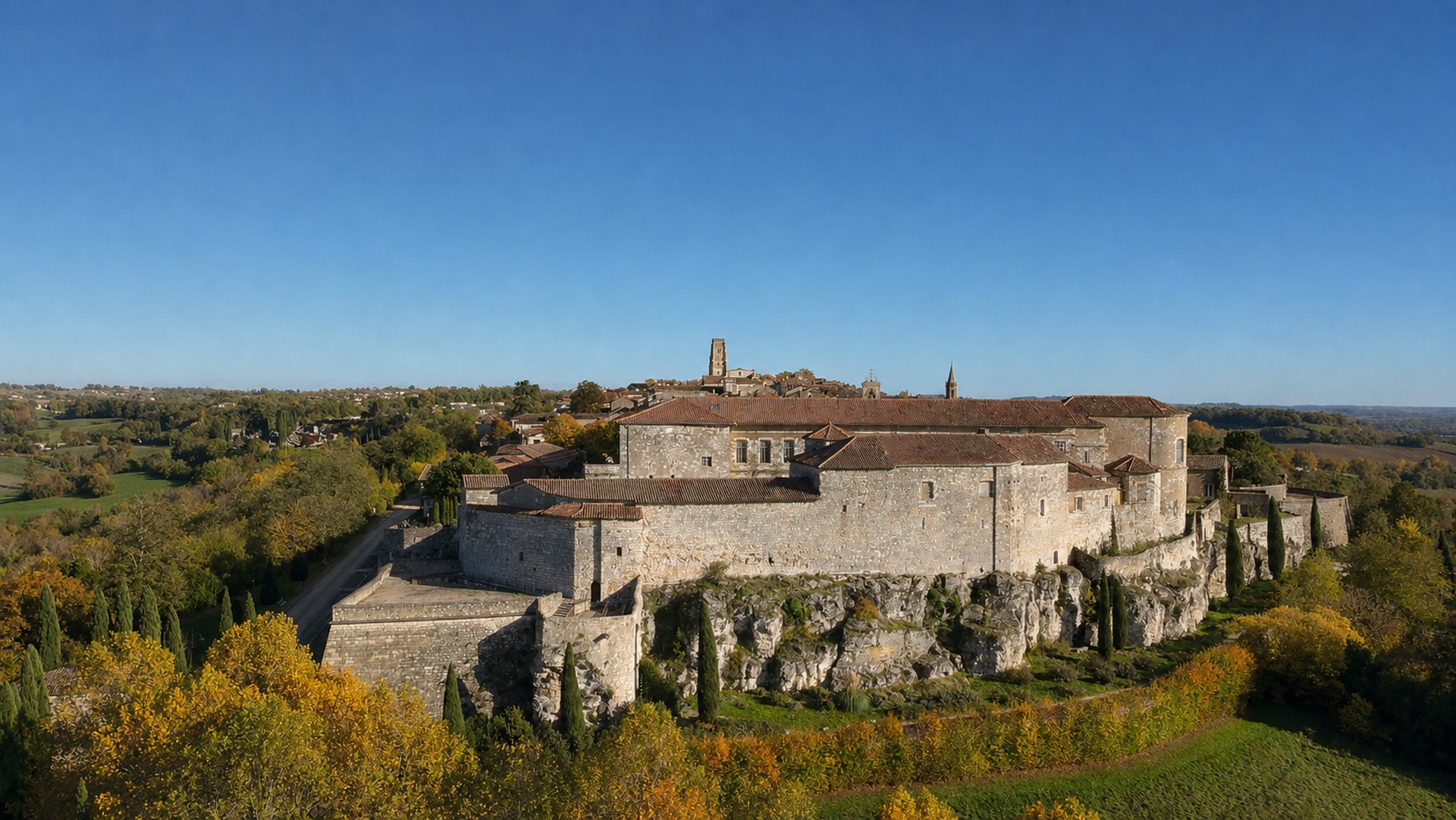 Les remparts et les bâtiments de Lectoure sur leur escarpement rocheux, entourés de végétation automnale